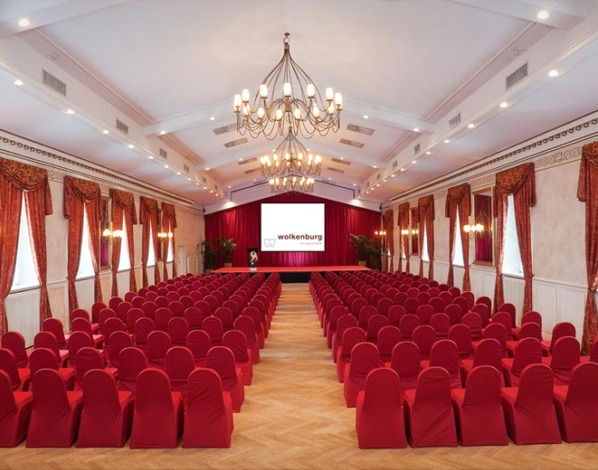 Bestuhlter Tagungsraum im Festsaal mit Bühne in rot gehalten.